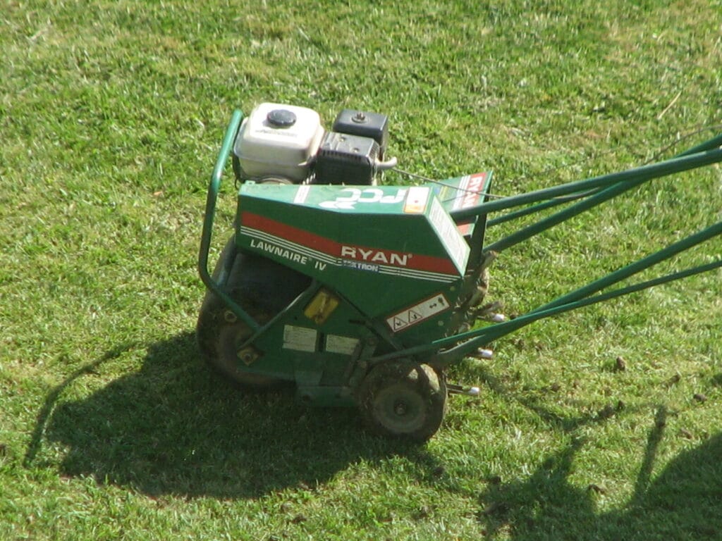 Green lawn aerator machine with white engine sits on healthy grass lawn